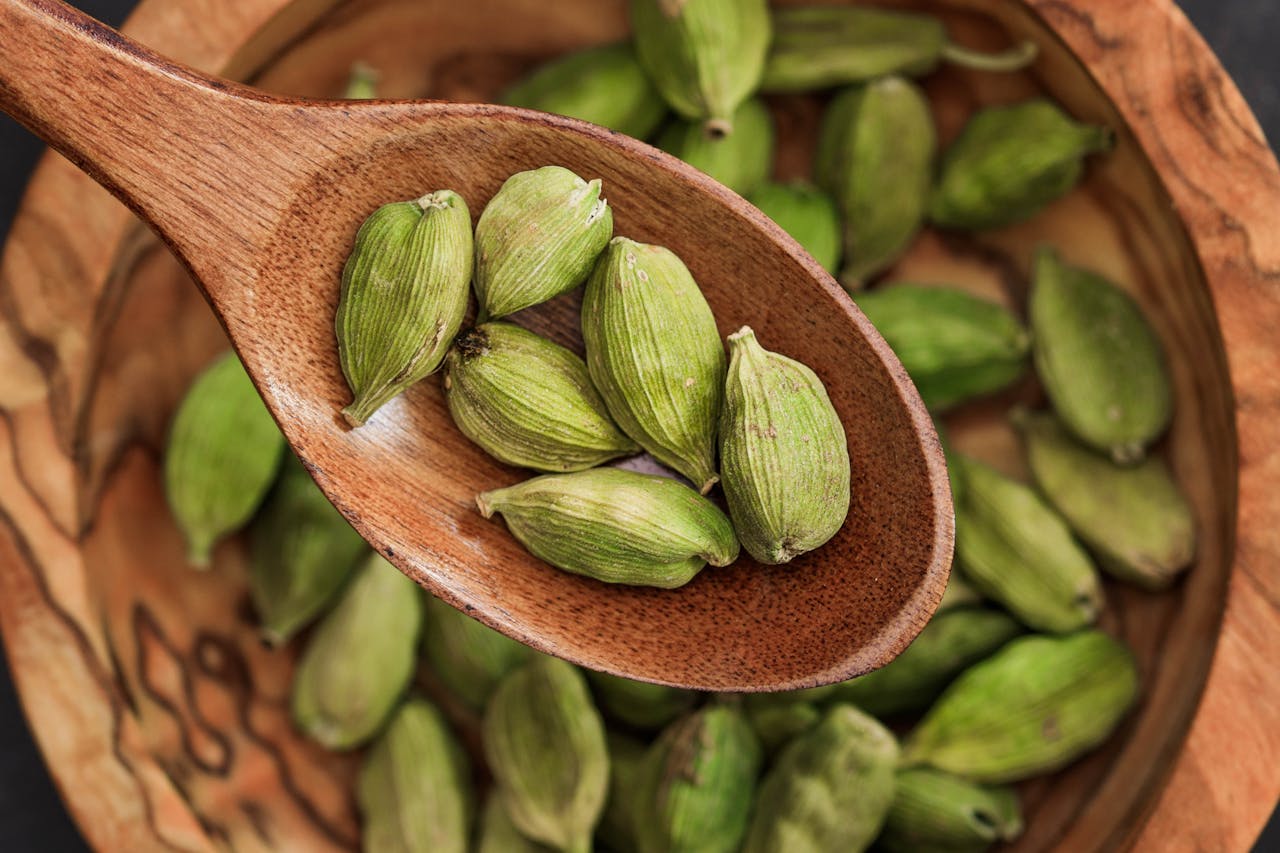Wooden spoon holding fresh green cardamom on rustic bowl. Ideal for culinary themes.